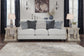 A neutral-toned living room with a light gray sofa, decorative pillows, two matching side tables with lamps, the Ogaleesha Wall Sconce in bronze-tone metal, and wall art above the sofa.