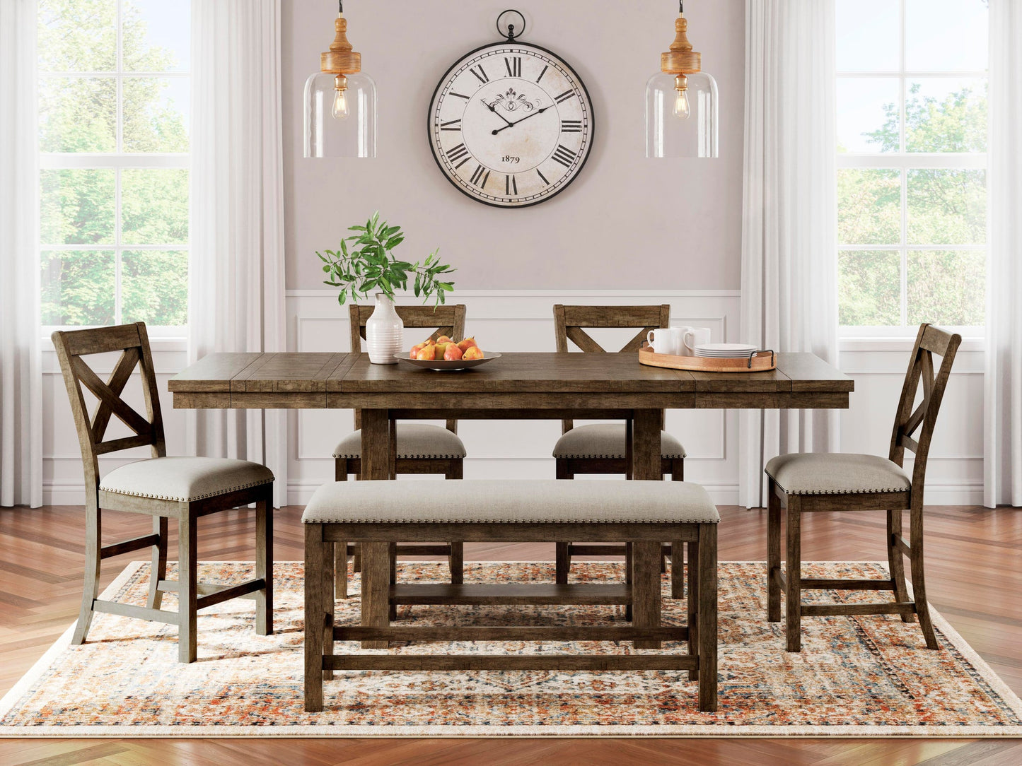 A wooden dining table, four chairs, and a bench sit on a patterned rug in a bright room, accented by pendant lights, a potted plant, and the Augustina Wall Clock with large Roman numerals on the wall.