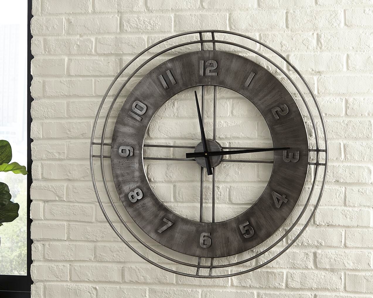 The Ana Sofia Wall Clock, a large metal round clock with a rustic finish and open center, is shown mounted on a white brick wall, displaying the time as 10:11.