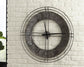 The Ana Sofia Wall Clock, a large metal round clock with a rustic finish and open center, is shown mounted on a white brick wall, displaying the time as 10:11.