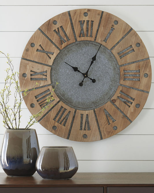 The Payson Wall Clock, featuring a wood and metal design with large Roman numerals, hangs above a table adorned with two ceramic vases and a small branch arrangement.