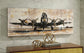 The Kalene Wall Art, featuring a vintage propeller airplane, hangs on a marble wall above a wooden cabinet decorated with gold spheres and stacked books.