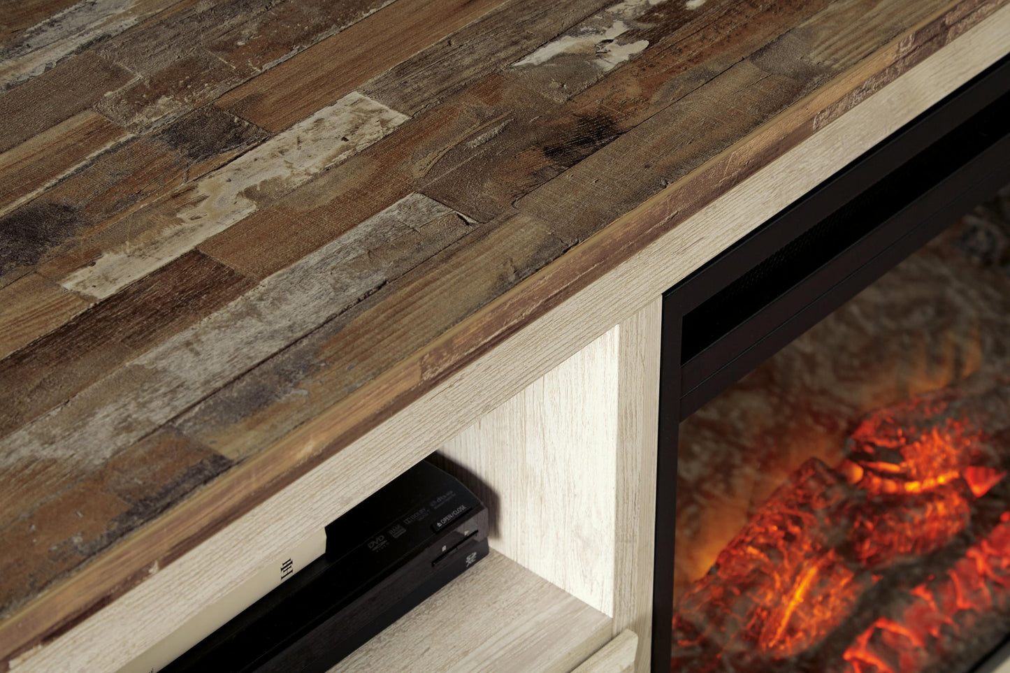 Close-up of the Willowton LG TV Stand w/Fireplace Option, showcasing its rustic whitewash finish, open shelf for electronics, and a partial view of the built-in electric fireplace with glowing embers.