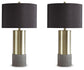 A pair of Jacek Metal Table Lamps featuring cylindrical brass-tone bases, textured faux concrete bottoms, and black drum shades are displayed side by side against a white background.